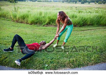 Stock Image - Young woman doing training and pulling boyfriend on grass. Fotosearch