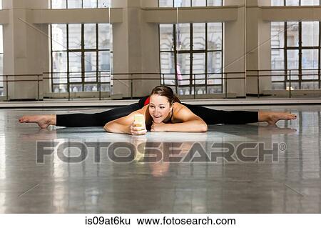 Stock Photograph - Young woman in dance studio doing the splits looking at smartphone smiling. Fotosearch