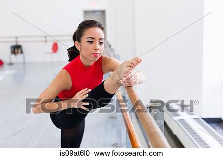Stock Image - Young woman in dance studio leg raised on barre. Fotosearch