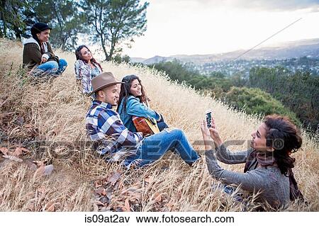 Young woman photographing her four adult siblings on grassy hill View Large Photo Image Stock Photo - Young woman photographing her four adult siblings on grassy hill. Fotosearch