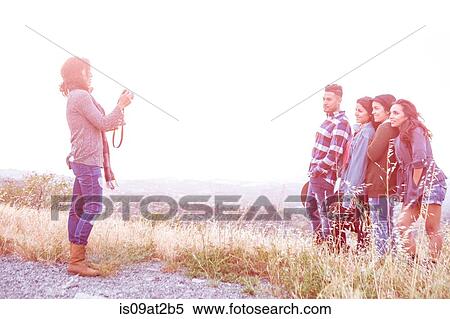 Stock Photography - Young woman photographing her four adult siblings on rural hill. Fotosearch