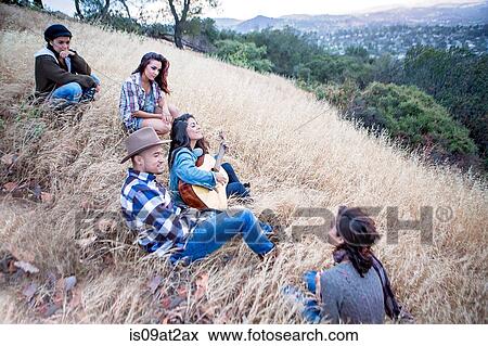 Young woman playing guitar for adult siblings on grassy hill View Large Photo Image Stock Photo - Young woman playing guitar for adult siblings on grassy hill. Fotosearch