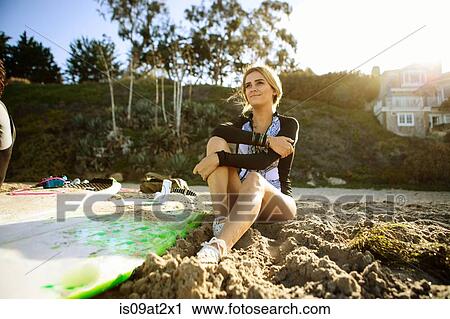 "Young woman sitting on sand, surfboard beside her" View Large Photo Image Stock Image - "Young woman sitting on sand, surfboard beside her". Fotosearch