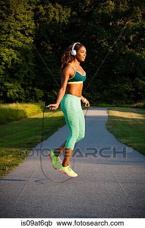 Stock Image - Young woman training with skipping rope on path. Fotosearch