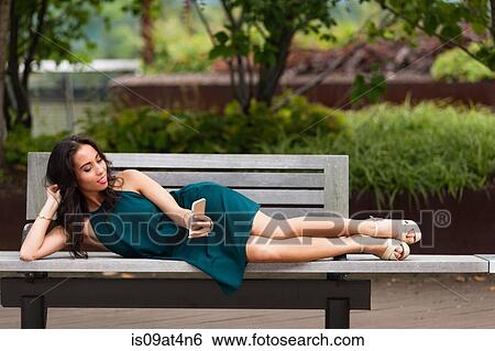 Young woman using smartphone on park bench View Large Photo Image Stock Photograph - Young woman using smartphone on park bench. Fotosearch