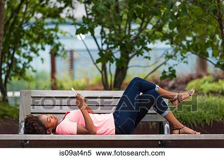 Young woman using smartphone on park bench View Large Photo Image Stock Photography - Young woman using smartphone on park bench. Fotosearch