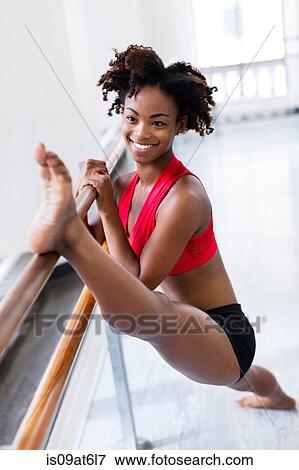 Stock Photo - Young woman with leg raised on barre looking at camera smiling. Fotosearch