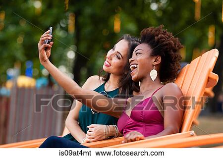 Stock Photograph - Young women taking selfie in deck chair. Fotosearch