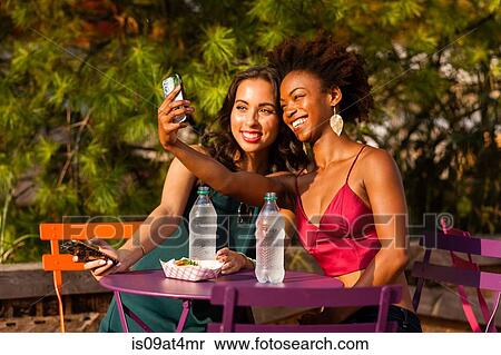Young women taking selfie on bench View Large Photo Image Stock Photography - Young women taking selfie on bench. Fotosearch