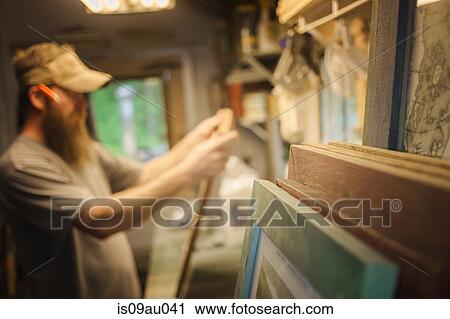 Stock Image - Artist working in workshop, wooden frames in foreground. Fotosearch