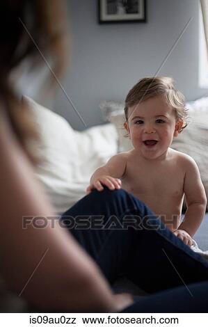 Stock Photo - Baby boy holding mothers leg looking at camera smiling. Fotosearch