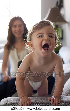Baby boy holding onto sofa looking at camera open mouthed View Large Photo Image Stock Photograph - Baby boy holding onto sofa looking at camera open mouthed. Fotosearch