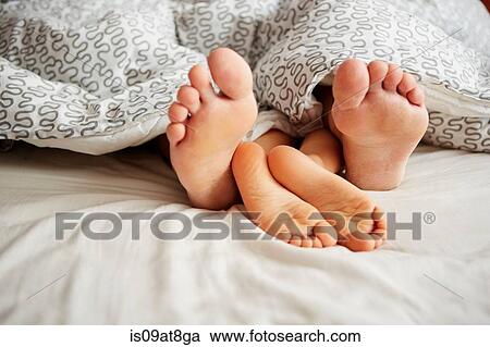 Stock Image - Bare feet of father and son lying in bed. Fotosearch