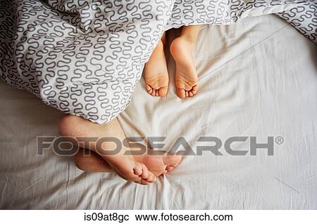 Stock Image - Bare feet of father and young son lying in bed. Fotosearch