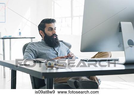 Bearded businessman sitting in front of computer View Large Photo Image Stock Photo - Bearded businessman sitting in front of computer. Fotosearch