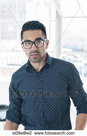 Stock Image - Bespectacled businessman by office window. Fotosearch