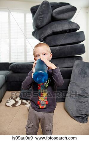 Stock Photo - Boy drinking in living room, pile of cushions in background. Fotosearch