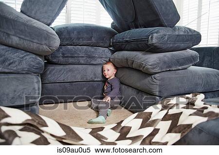Stock Photography - Boy leaning against pile of cushions in living room. Fotosearch