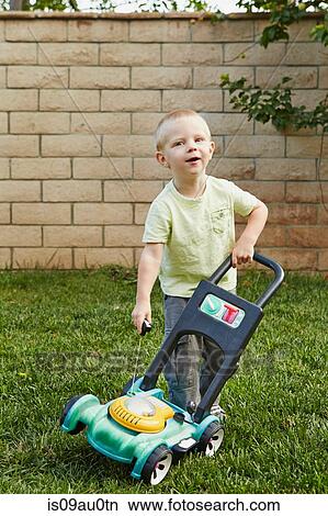 Picture - Boy playing with toy lawnmower in backyard. Fotosearch