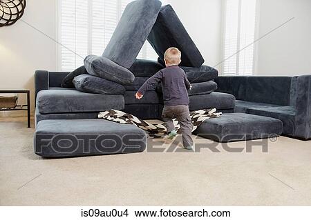 Picture - Boy running towards pile of cushions in living room. Fotosearch