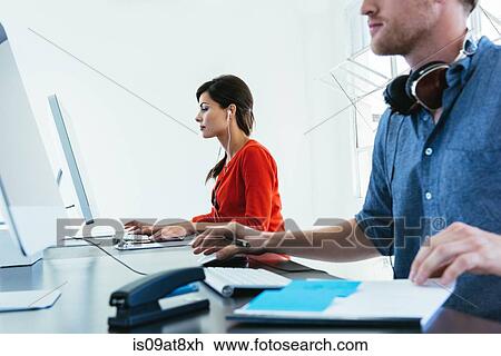 Stock Image - Business people working on computer by office window. Fotosearch