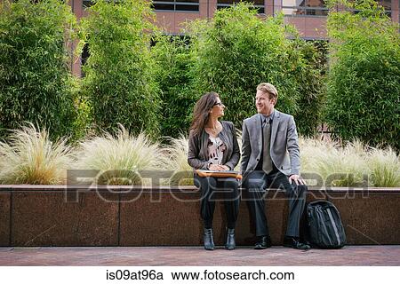 Businessman and woman in city sitting on wall chatting View Large Photo Image Stock Image - Businessman and woman in city sitting on wall chatting. Fotosearch