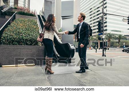 Stock Image - Businessman and woman shaking hands in city. Fotosearch