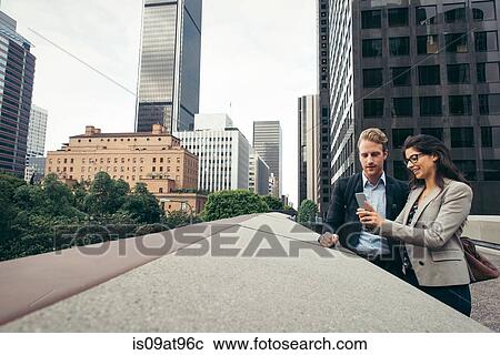 Stock Image - Businessman and woman sharing smartphone texts, Los Angeles, USA. Fotosearch