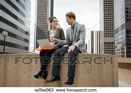 Businessman and woman sitting on wall using laptop, Los Angeles, USA View Large Photo Image Stock Image - Businessman and woman sitting on wall using laptop, Los Angeles, USA. Fotosearch