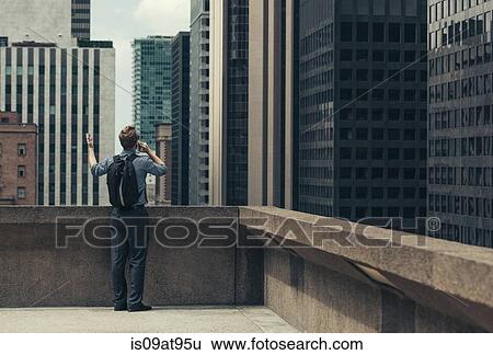 Stock Photograph - Businessman on rooftop talking on smartphone, Los Angeles, USA. Fotosearch