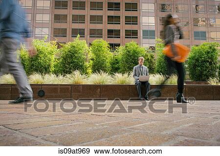 Businessman sitting on wall outside office using laptop View Large Photo Image Stock Photo - Businessman sitting on wall outside office using laptop. Fotosearch