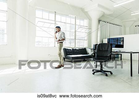 Stock Image - Businessman speaking on smartphone by office window. Fotosearch