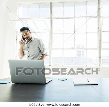 Businessman speaking on smartphone by office window View Large Photo Image Stock Image - Businessman speaking on smartphone by office window. Fotosearch