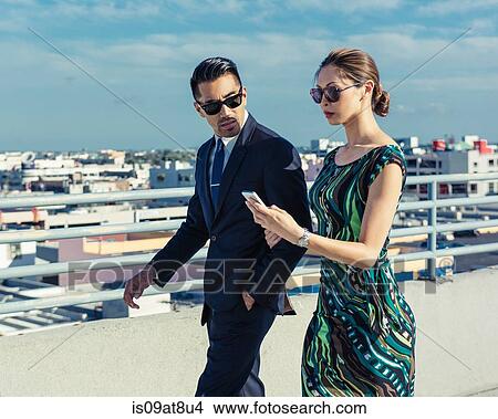 Businessman with businesswoman using smartphone on roof terrace, Los Angeles, California, USA View Large Photo Image Picture - Businessman with businesswoman using smartphone on roof terrace, Los Angeles, California, USA. Fotosearch