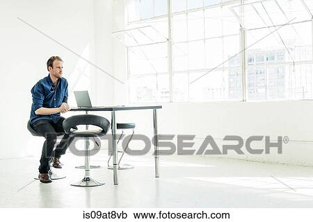 Stock Image - Businessman working on laptop by office window. Fotosearch