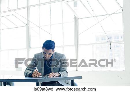 Stock Image - Businessman writing notes on table by office window. Fotosearch