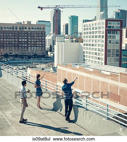 Stock Image - Businesspeople looking and pointing at buildings on roof terrace, Los Angeles, California, USA. Fotosearch