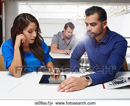 Stock Photo - Businesswoman and businessman sitting at desk, looking at digital tablet. Fotosearch
