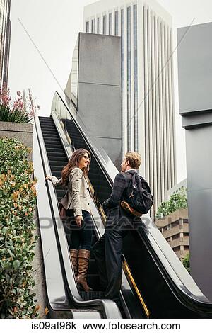 Stock Image - Businesswoman and man moving up escalator, Los Angeles, USA. Fotosearch