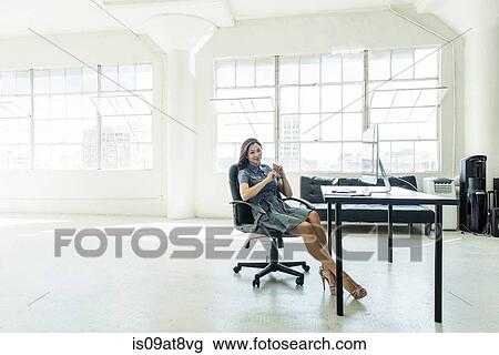 Stock Image - Businesswoman resting on chair by office window. Fotosearch