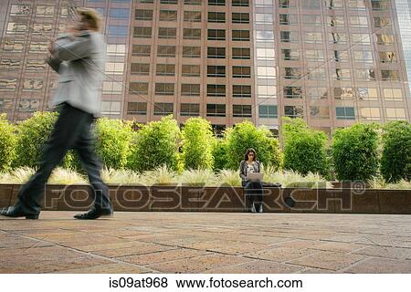 Stock Photo - Businesswoman sitting on wall outside office using laptop. Fotosearch