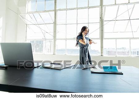 Businesswoman speaking on smartphone by office window View Large Photo Image Stock Photo - Businesswoman speaking on smartphone by office window. Fotosearch