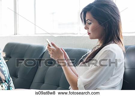 Businesswoman using smartphone on sofa by office window View Large Photo Image Stock Photo - Businesswoman using smartphone on sofa by office window. Fotosearch