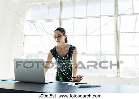 Businesswoman working on laptop by office window View Large Photo Image Stock Photograph - Businesswoman working on laptop by office window. Fotosearch