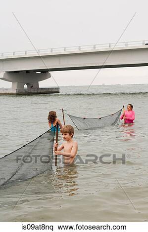 Stock Photography - Children in ocean holding fishing nets and Sanibel causeway bridge, Sanibel Island, Pine Island Sound, Florida, USA. Fotosearch