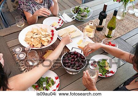 Stock Image - Cropped overhead view of female friends eating lunch on patio. Fotosearch