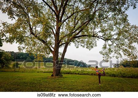 Stock Photo - Distant view of young woman practicing yoga pose in rural park. Fotosearch