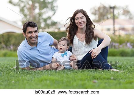 Stock Photo - Family with baby boy sitting on grass looking at camera smiling. Fotosearch