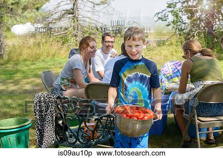 Stock Photography - Family with young boy holding colander of tomatoes looking at camera smiling. Fotosearch