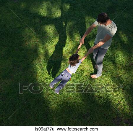 Stock Photograph - Father swinging son around, outdoors, elevated view. Fotosearch